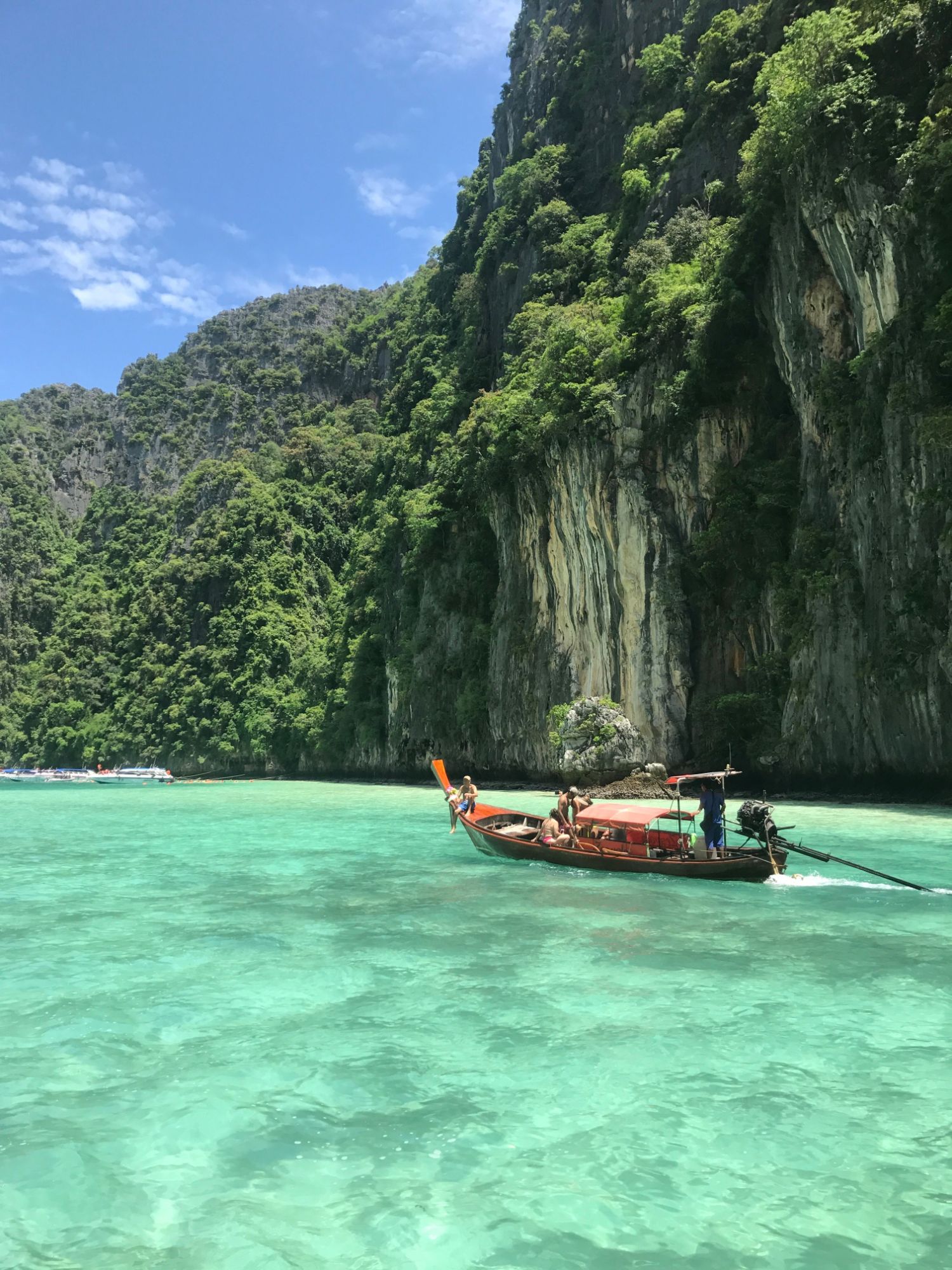 Traditional Thai longtail boat in the turquoise water of Phi Phi with limestone cliffs behind